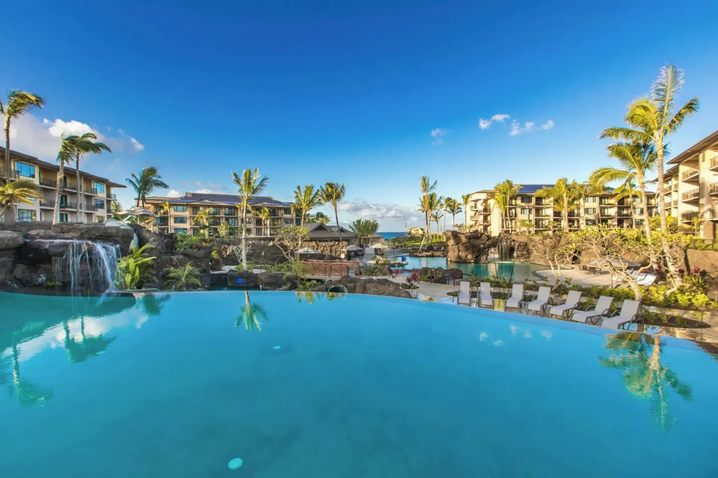 Wide resort pool with waterfalls, palms, lounge chairs, and buildings at Koloa Landing Resort at Poipu.