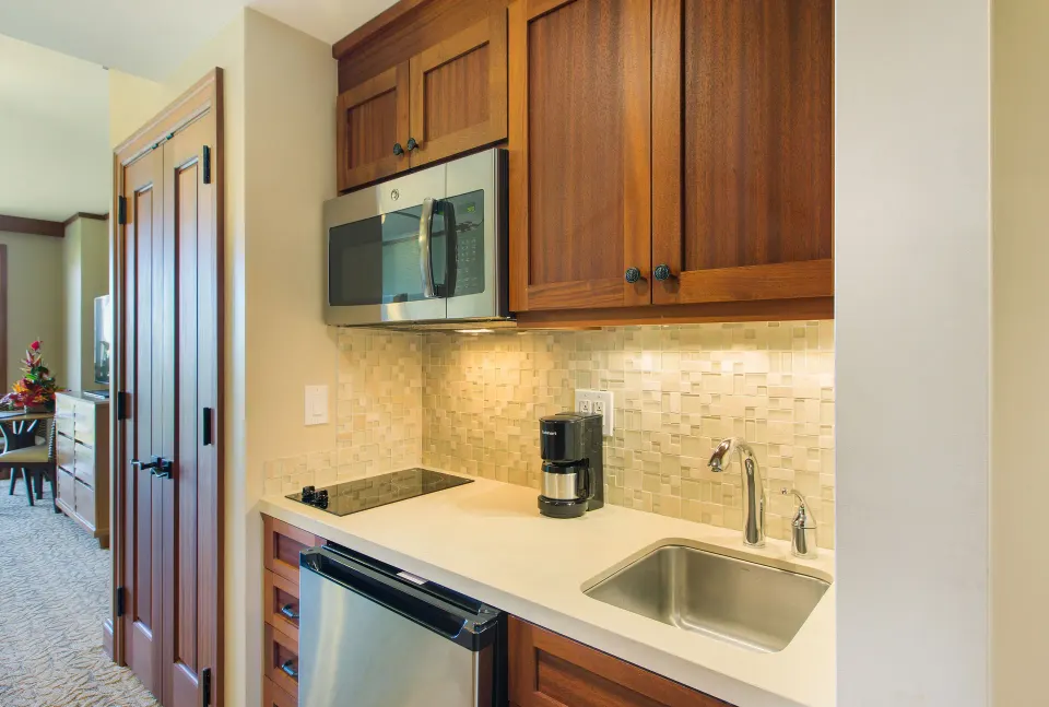 Studio kitchenette with sink, cooktop, microwave and wood cabinets at Koloa Landing Resort at Poipu.