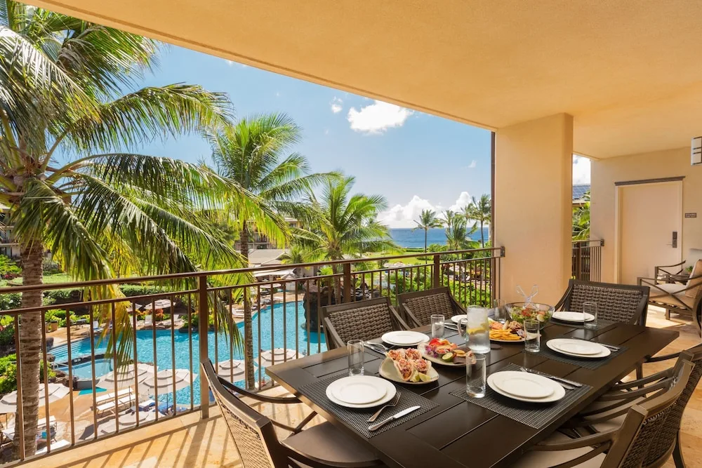 Covered villa balcony with dining table, pool, palms, and ocean beyond at Koloa Landing Resort at Poipu.