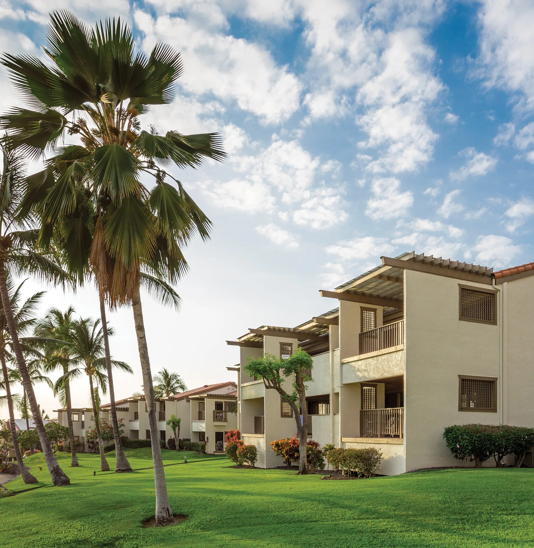 Balconied guest buildings and palms under a bright sky at Kona Coast Resort.
