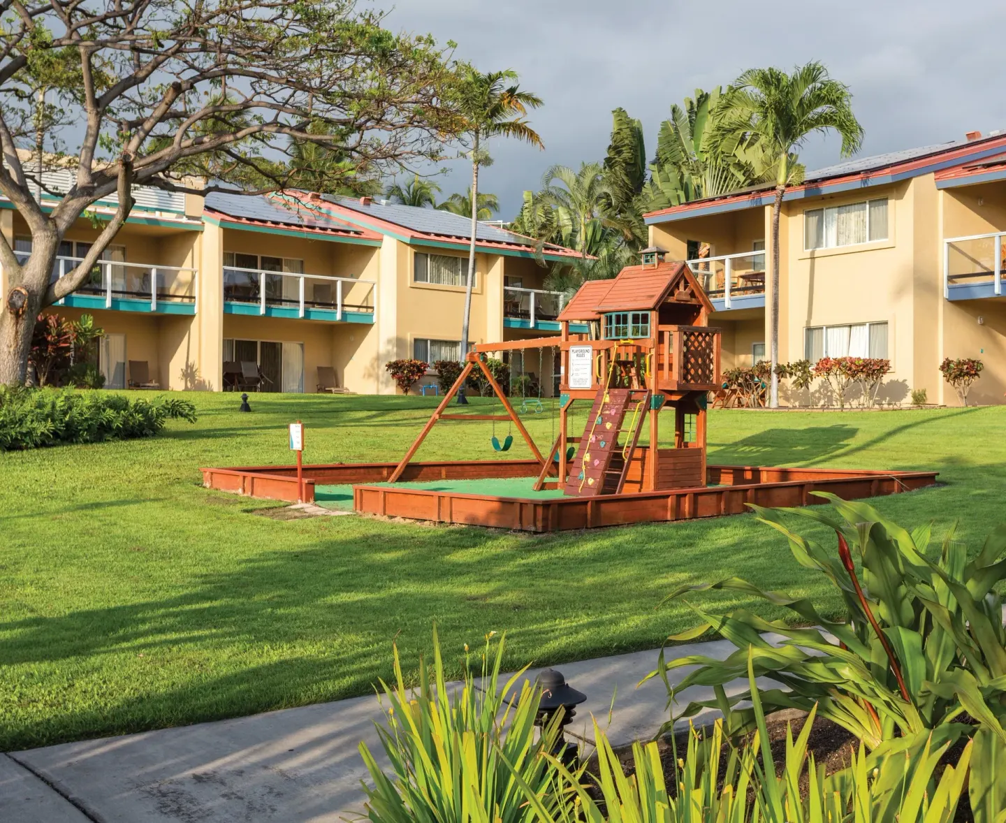 Children's play structure on a lawn between guest buildings at Kona Coast Resort.