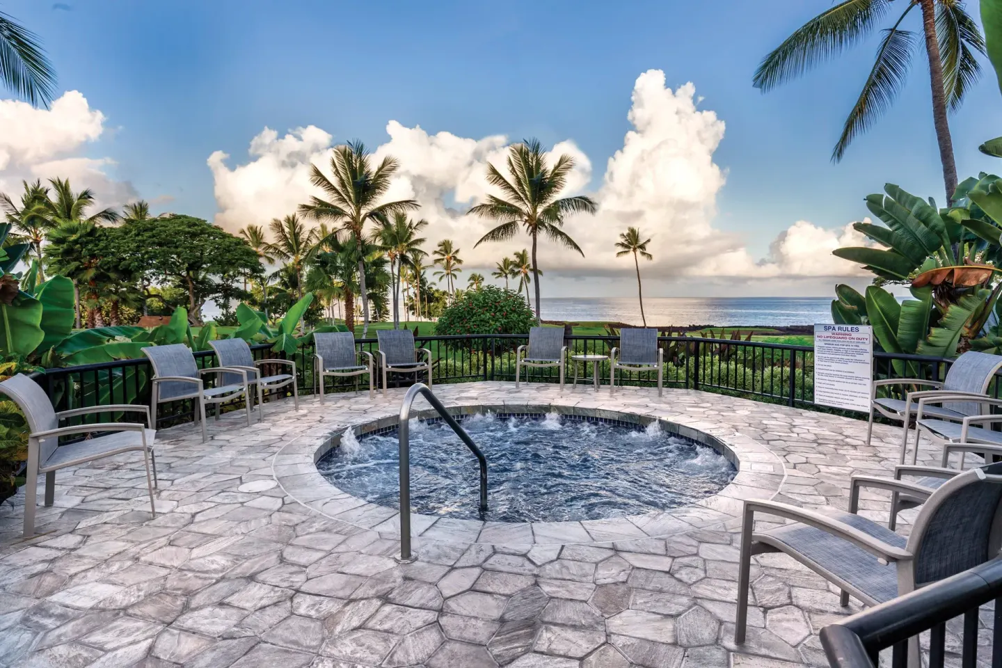Circular bubbling spa with lounge chairs, palms, and ocean view at Kona Coast Resort.