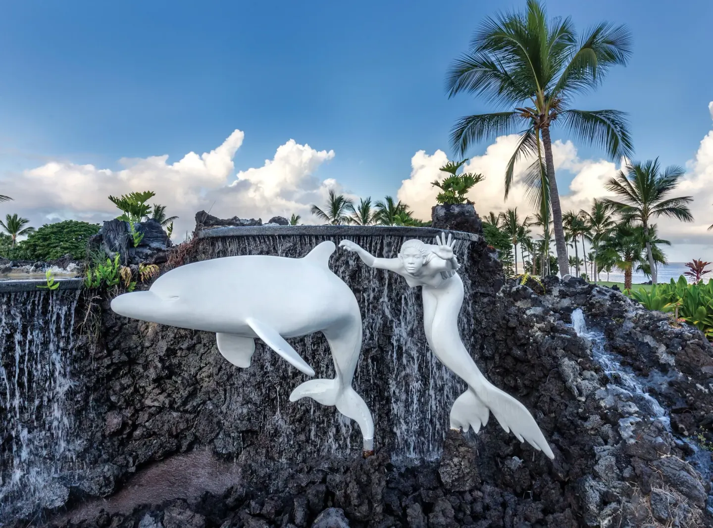 White dolphin and swimmer sculptures stand before a lava rock waterfall at Kona Coast Resort.