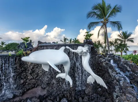 White dolphin and swimmer sculptures stand before a lava rock waterfall at Kona Coast Resort.