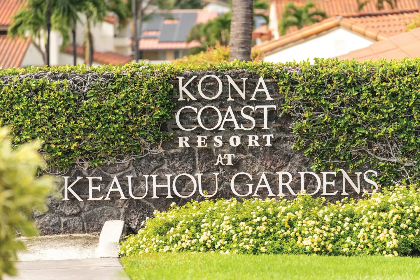 Kona Coast Resort entrance sign set in a hedge and stone wall with tropical landscaping.