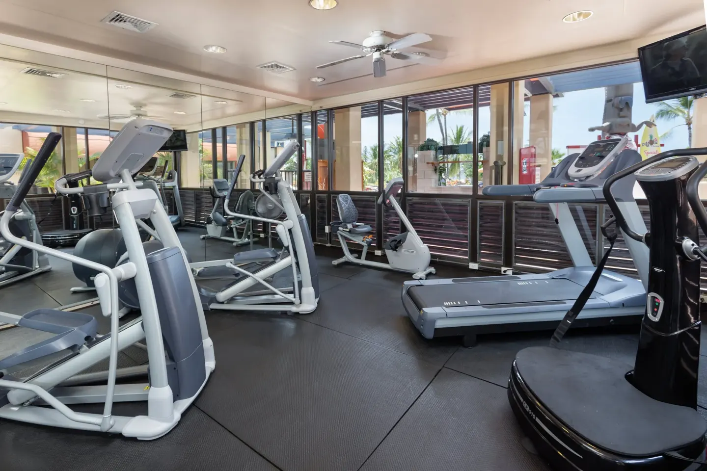 Fitness room with cardio machines, mirrors, windows, and a TV at Kona Coast Resort.