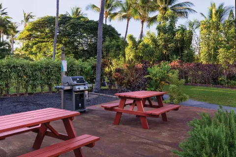 Red picnic tables and a gas grill sit in a garden barbecue area at Kona Coast Resort.