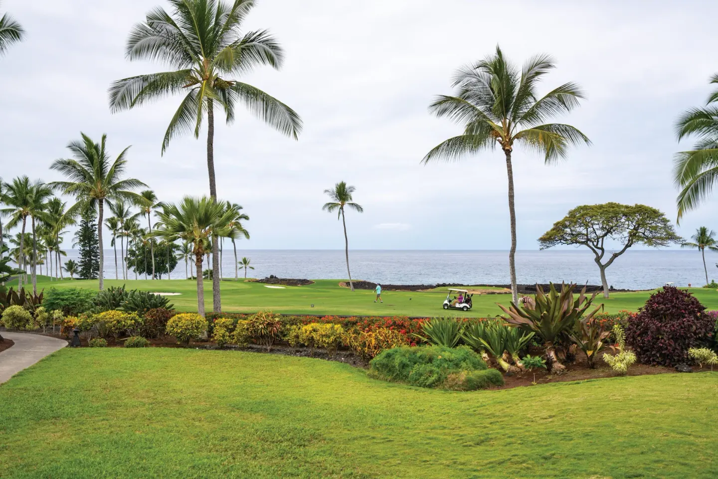 Oceanfront golf greens with palm trees and a cart near Kona Coast Resort.