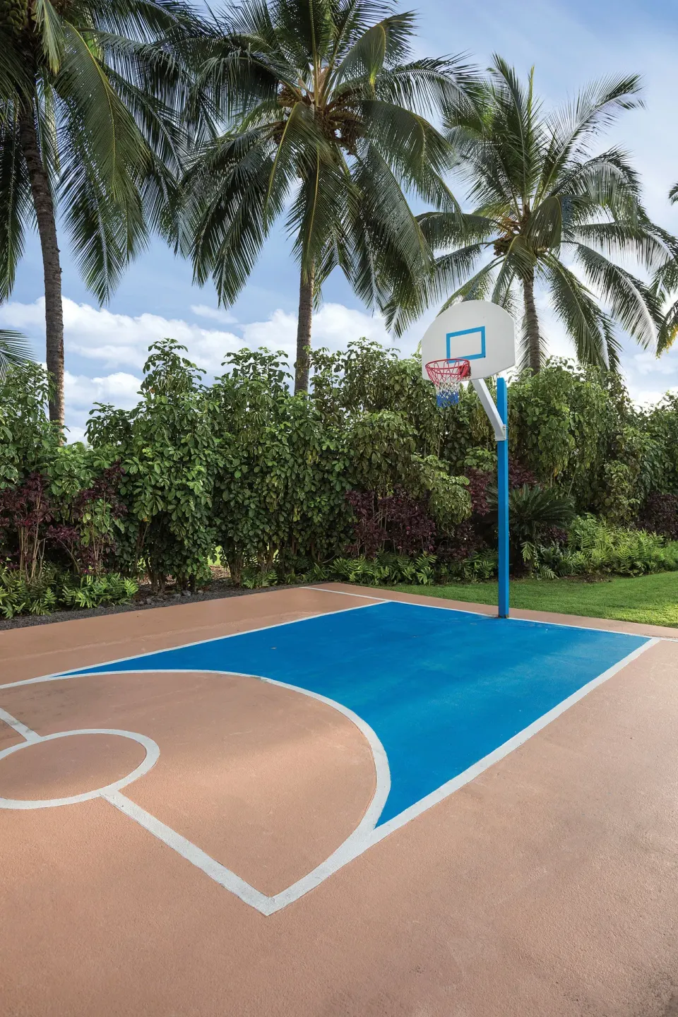 An outdoor basketball hoop and painted court sit beneath palm trees at Kona Coast Resort.