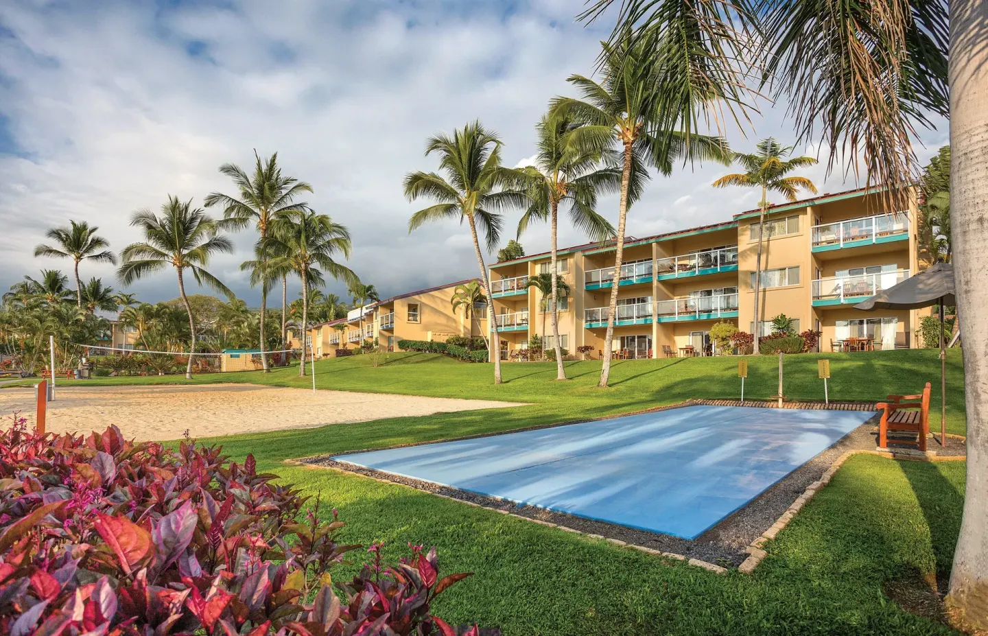 Sand volleyball court, blue game court, palms, and resort buildings at Kona Coast Resort.