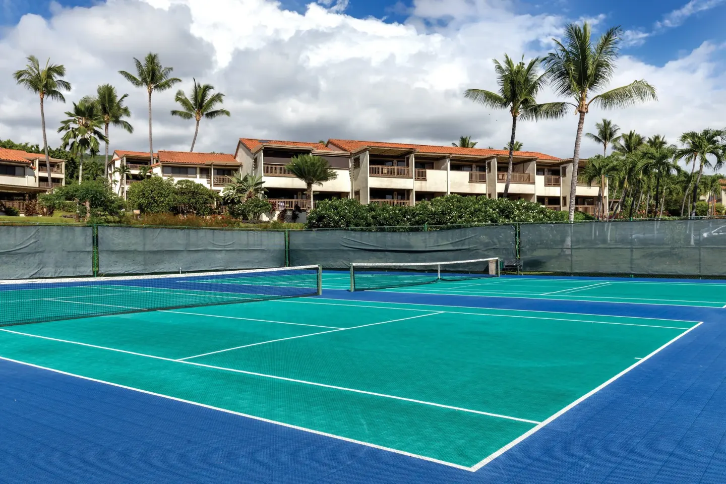 Outdoor sport courts with nets, palms, and resort buildings beyond at Kona Coast Resort.