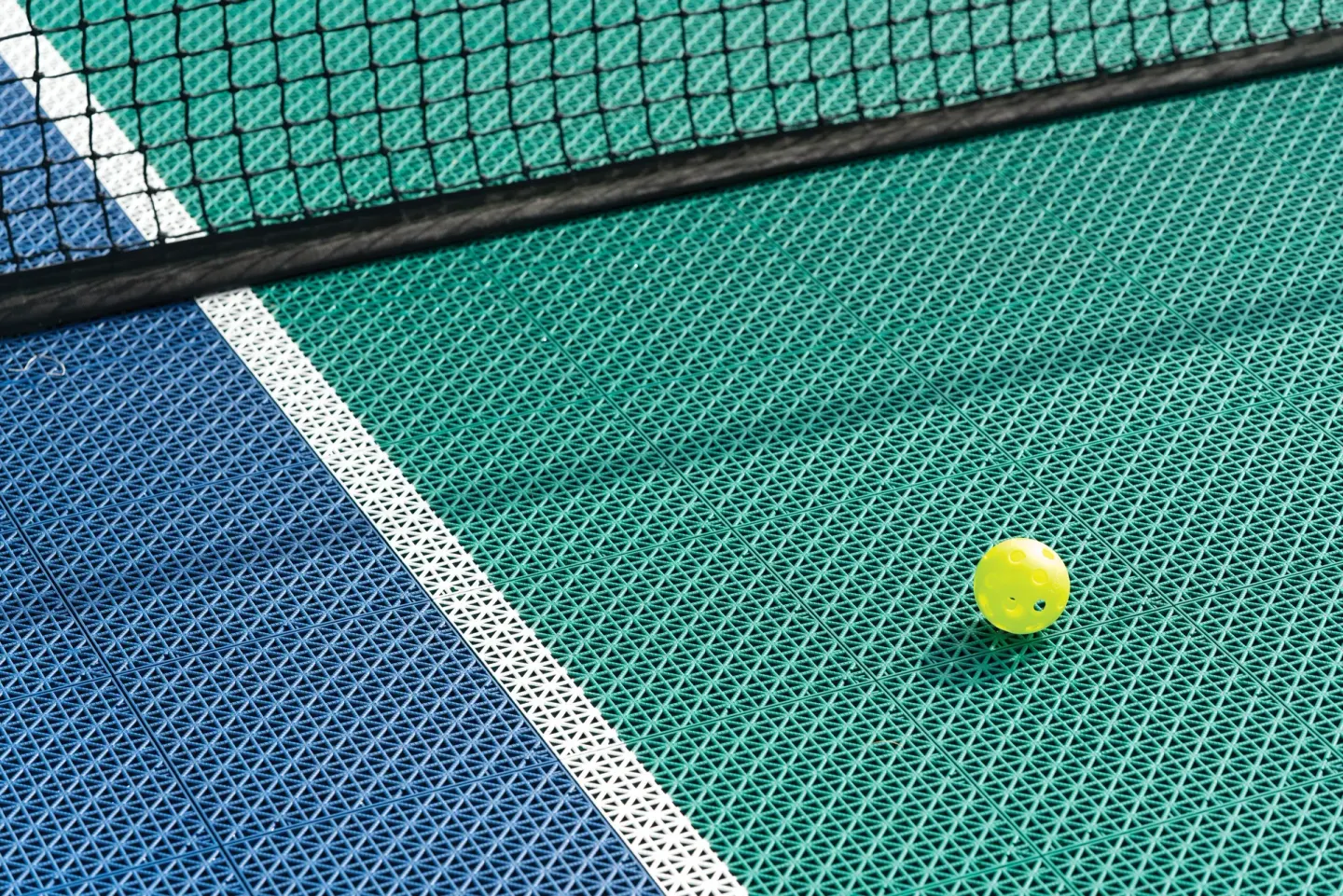 Yellow pickleball on a textured court surface near the net at Kona Coast Resort.
