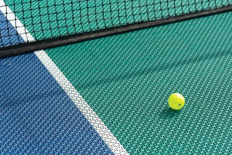 Yellow pickleball on a textured court surface near the net at Kona Coast Resort.