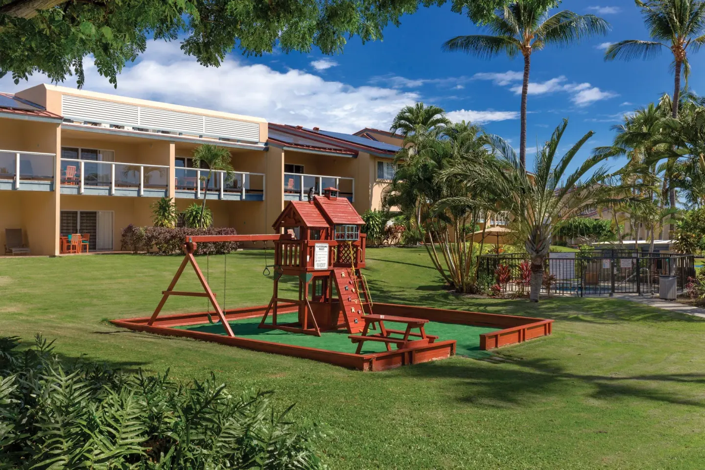 Wooden playground, lawn, palms, and guest buildings at Kona Coast Resort.