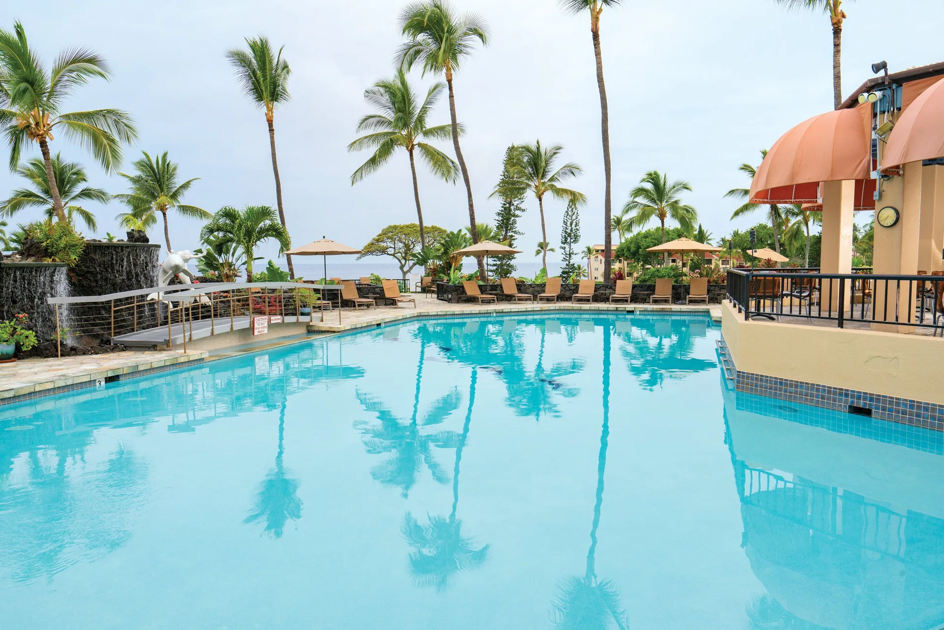 Outdoor pool with palm reflections and terrace awnings at Kona Coast Resort.