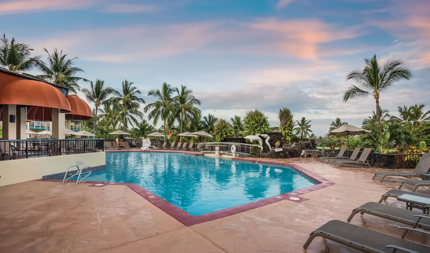 Resort pool with lounge chairs, palms, and pastel evening sky at Kona Coast Resort.