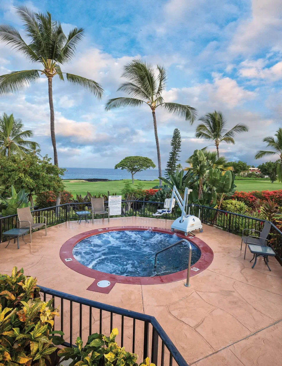 Round outdoor spa with lift, chairs, palms, lawn, and ocean beyond at Kona Coast Resort.