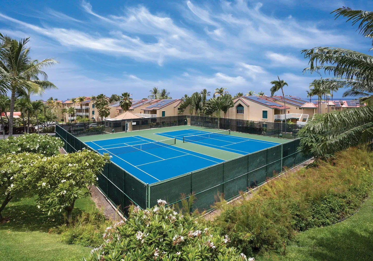 Blue tennis and pickleball courts bordered by palms and resort buildings at Kona Coast Resort.