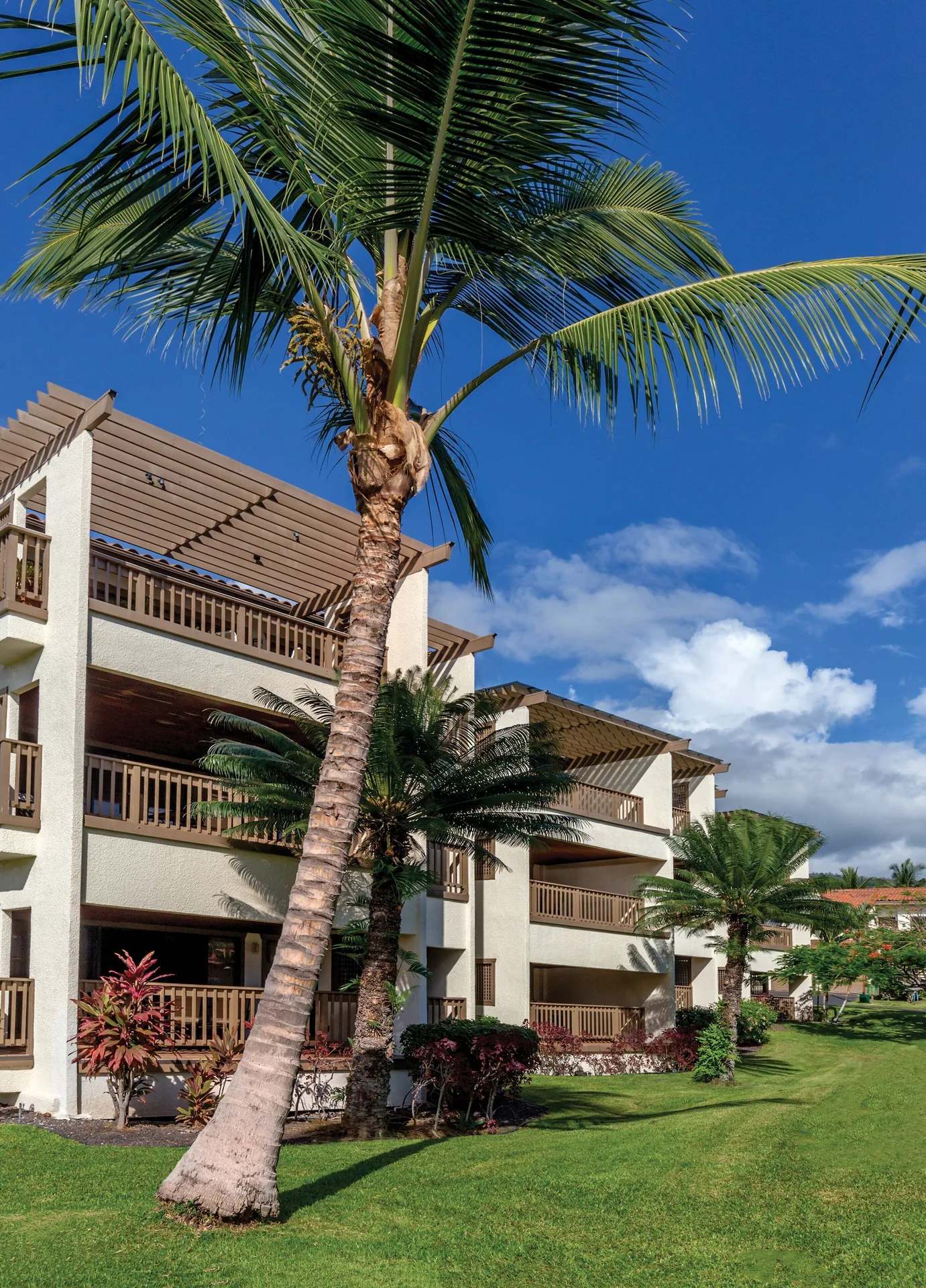 Three-story guest building with balconies and palms at Kona Coast Resort.