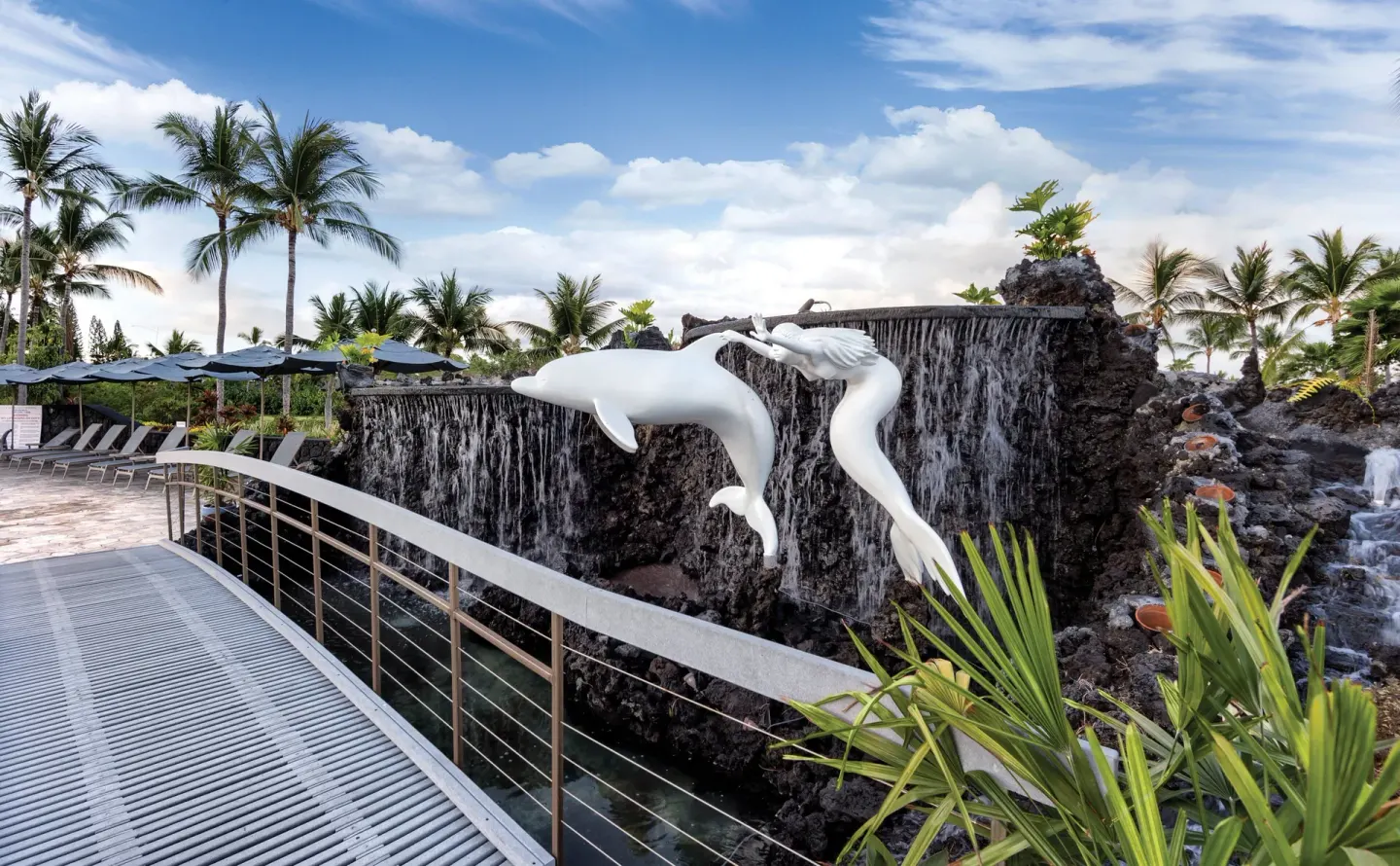 A bridge passes beside lava rock waterfalls and white sculptures at Kona Coast Resort.