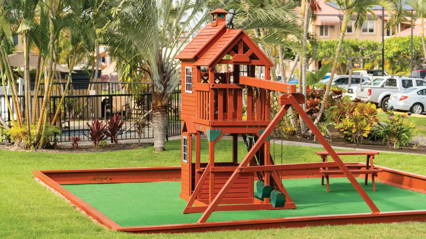 Wooden playhouse and swings in a tropical lawn area at Kona Coast Resort.