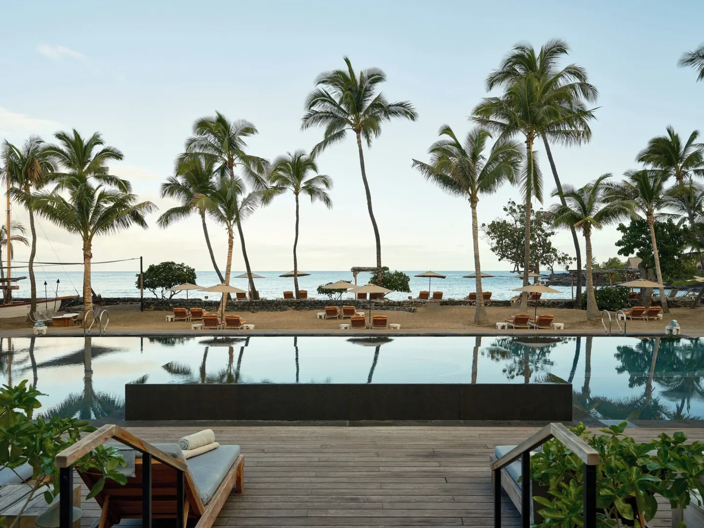 Calm pool, deck seating, beach umbrellas, palms and ocean at Kona Village.