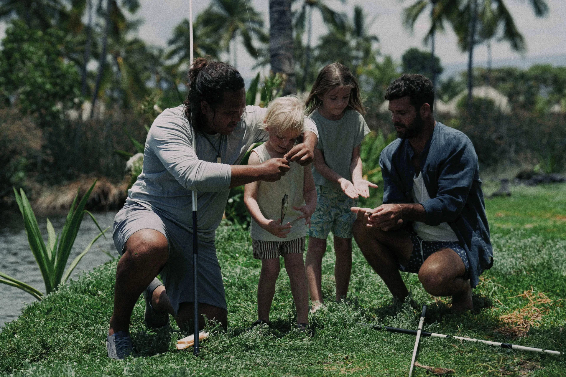 Adults and children gather with fishing rods beside a pond at Kona Village.
