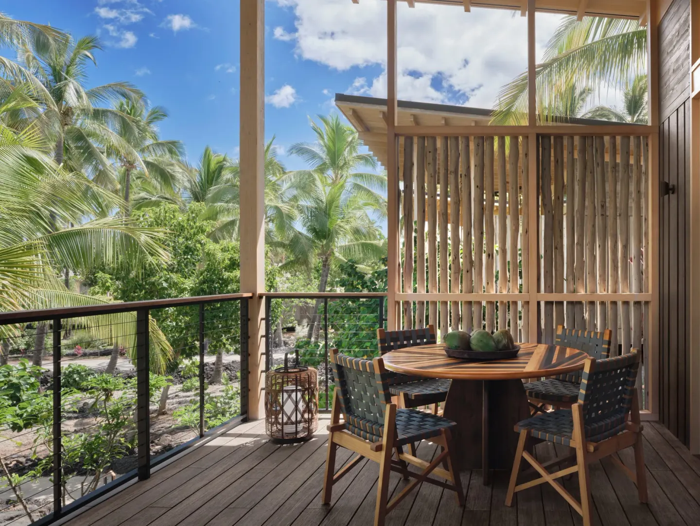 Lanai dining table framed by palms and a wood privacy screen at Kona Village.