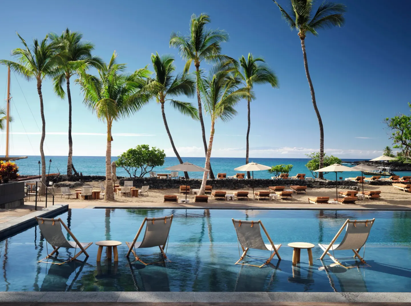 In-pool lounge chairs face palms, beach umbrellas and the ocean at Kona Village.