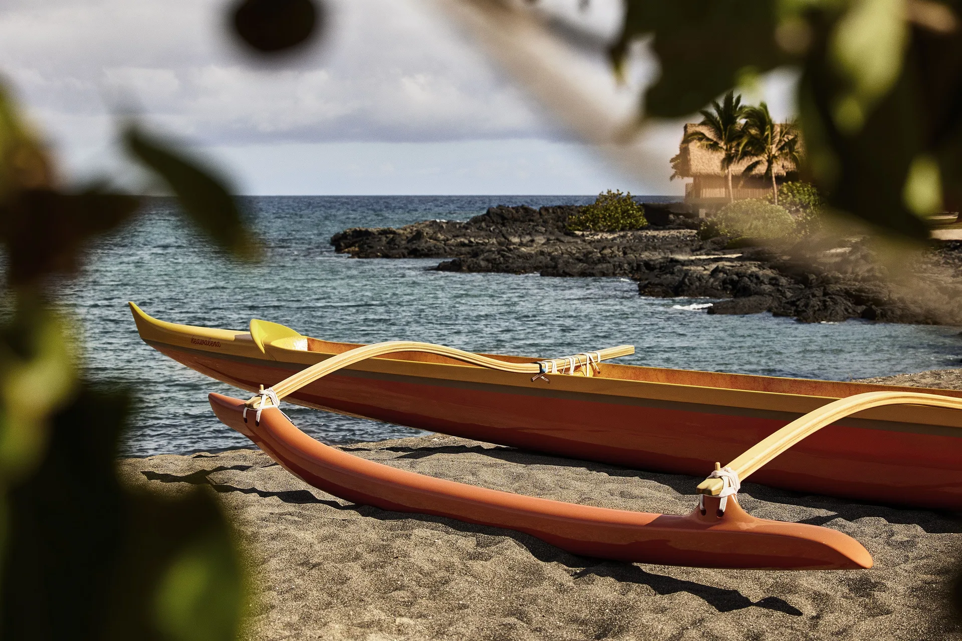 Outrigger canoe rests on the beach by rocky shoreline at Kona Village.