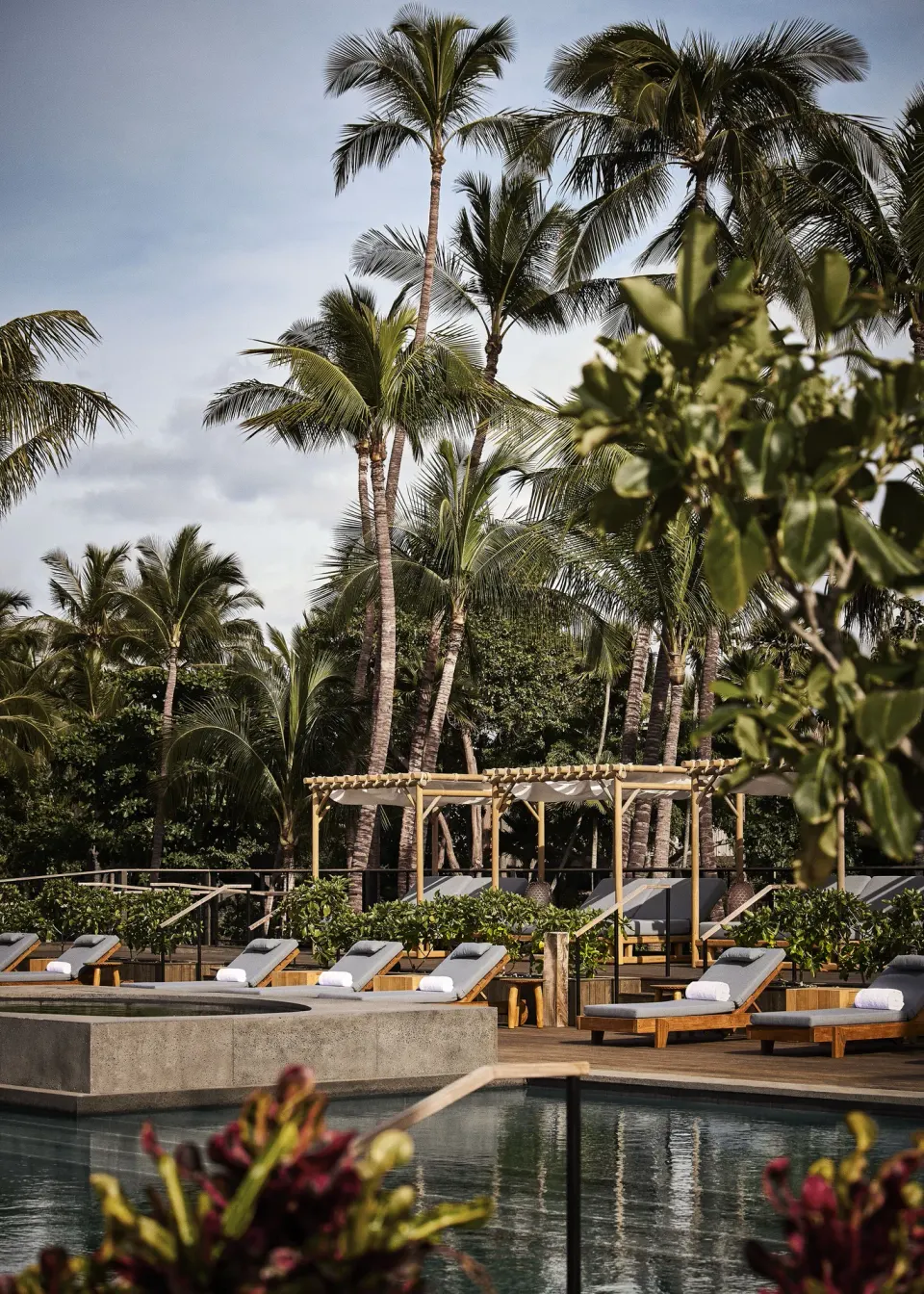 Pool deck with loungers, cabanas and tall palms at Kona Village.