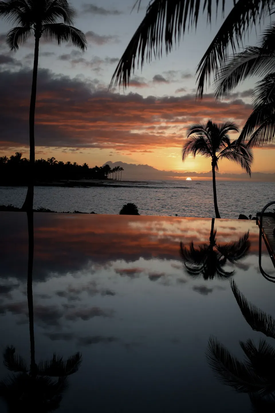 Sunset over the ocean reflected in the pool with palm silhouettes at Kona Village.
