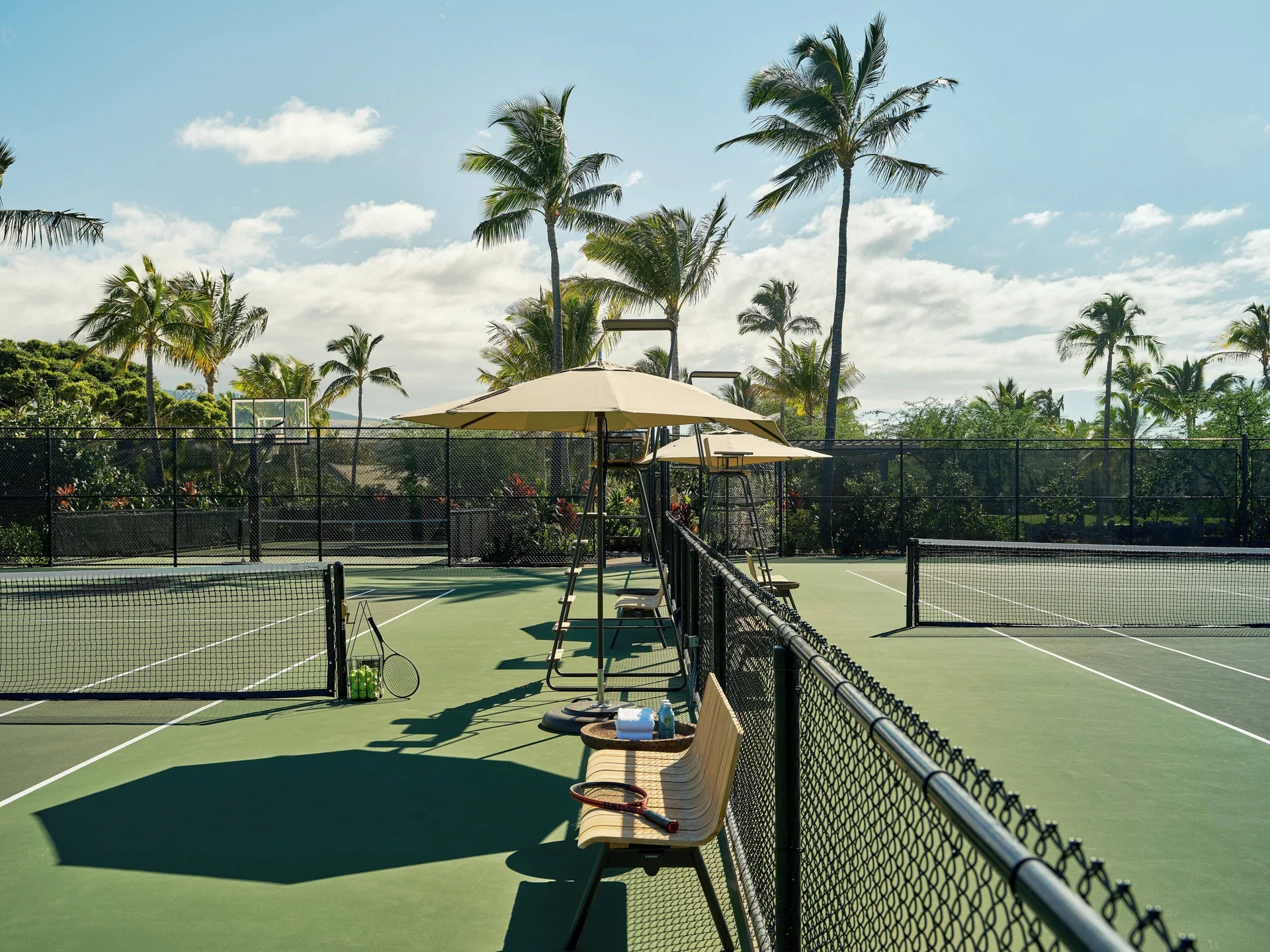 Tennis courts with nets, benches, umbrellas, and palms at Kona Village.