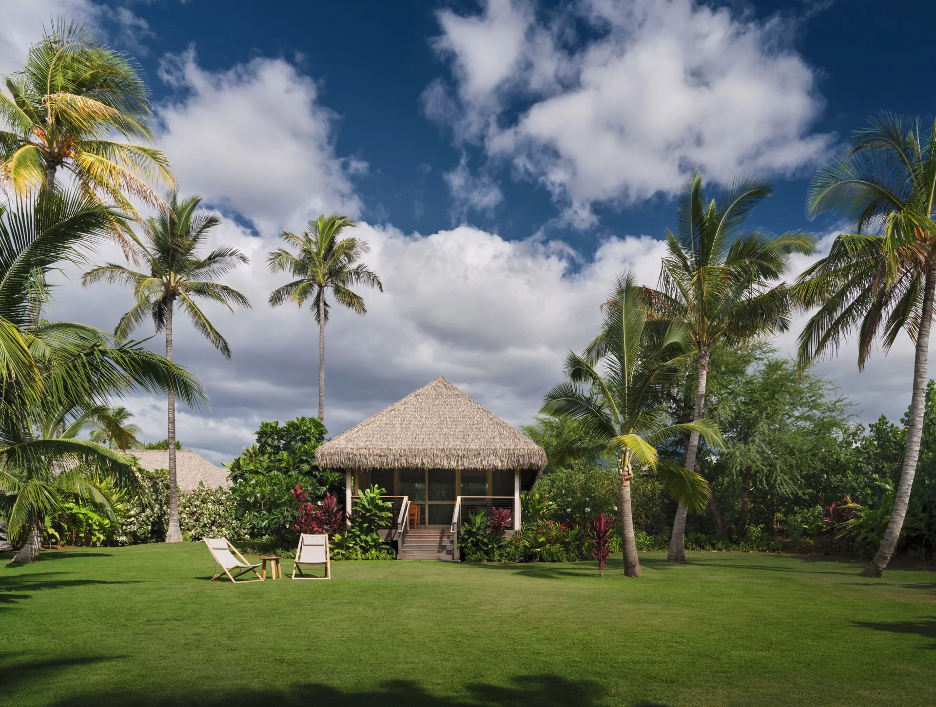 Thatched hale on a green lawn beneath palm trees at Kona Village.