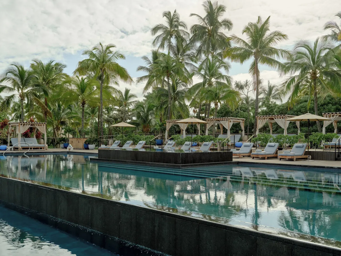 Tiered pool with cabanas, loungers and dense palm landscaping at Kona Village.