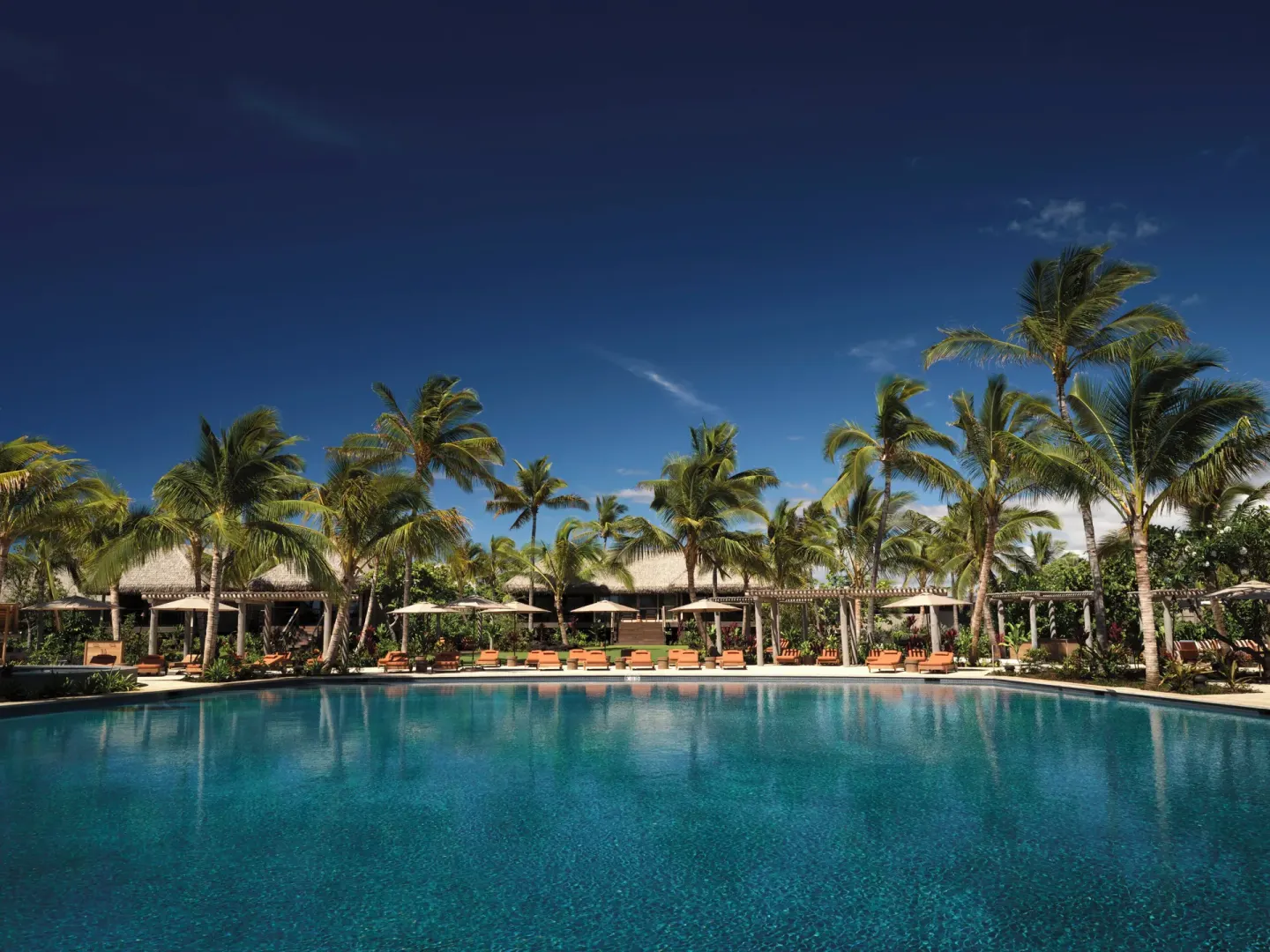 Wide resort pool bordered by palms and loungers at Kona Village.