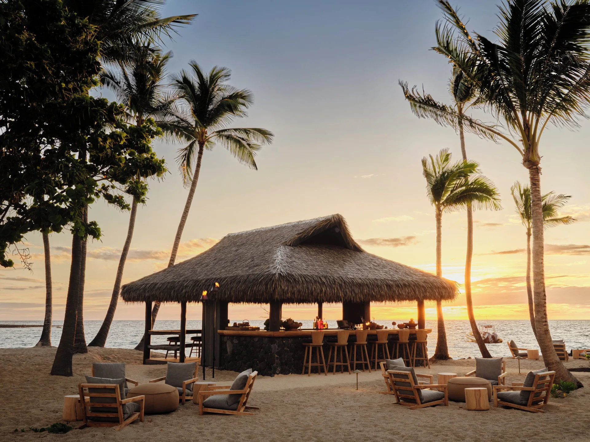 Beach bar under palms at sunset with lounge chairs at Kona Village.