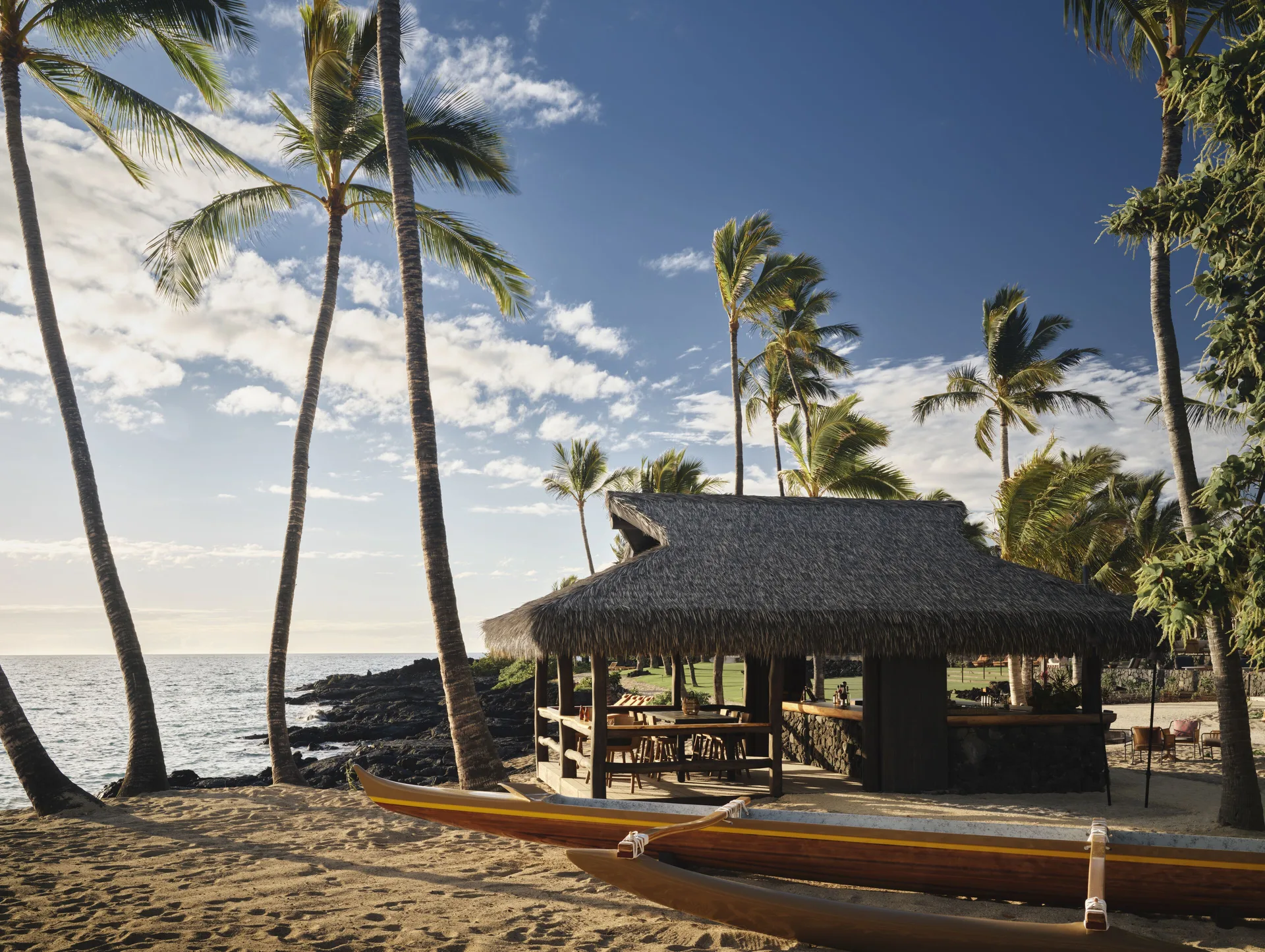 Thatched beach bar, outrigger canoe and palm trees by the ocean at Kona Village.