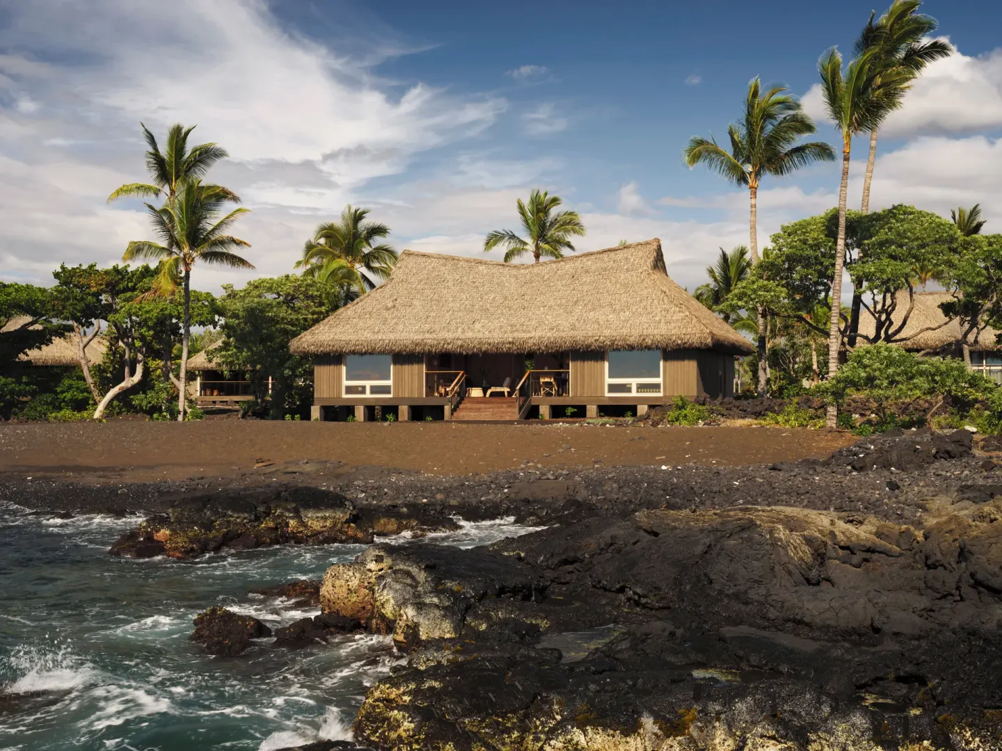 Thatched beachfront kauhale set behind black sand and lava rocks at Kona Village.