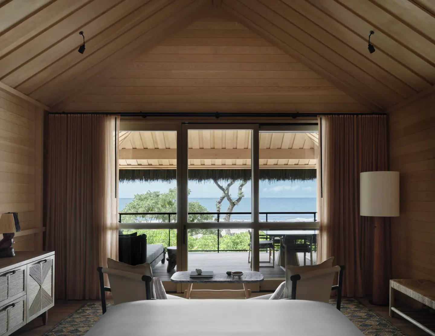 Beach Front Hale room with wood ceiling, bed, seating and ocean-facing lanai at Kona Village.