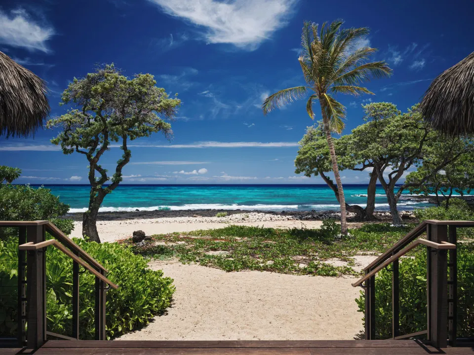 Beachfront kauhale entry with sand, palms, and ocean at Kona Village.