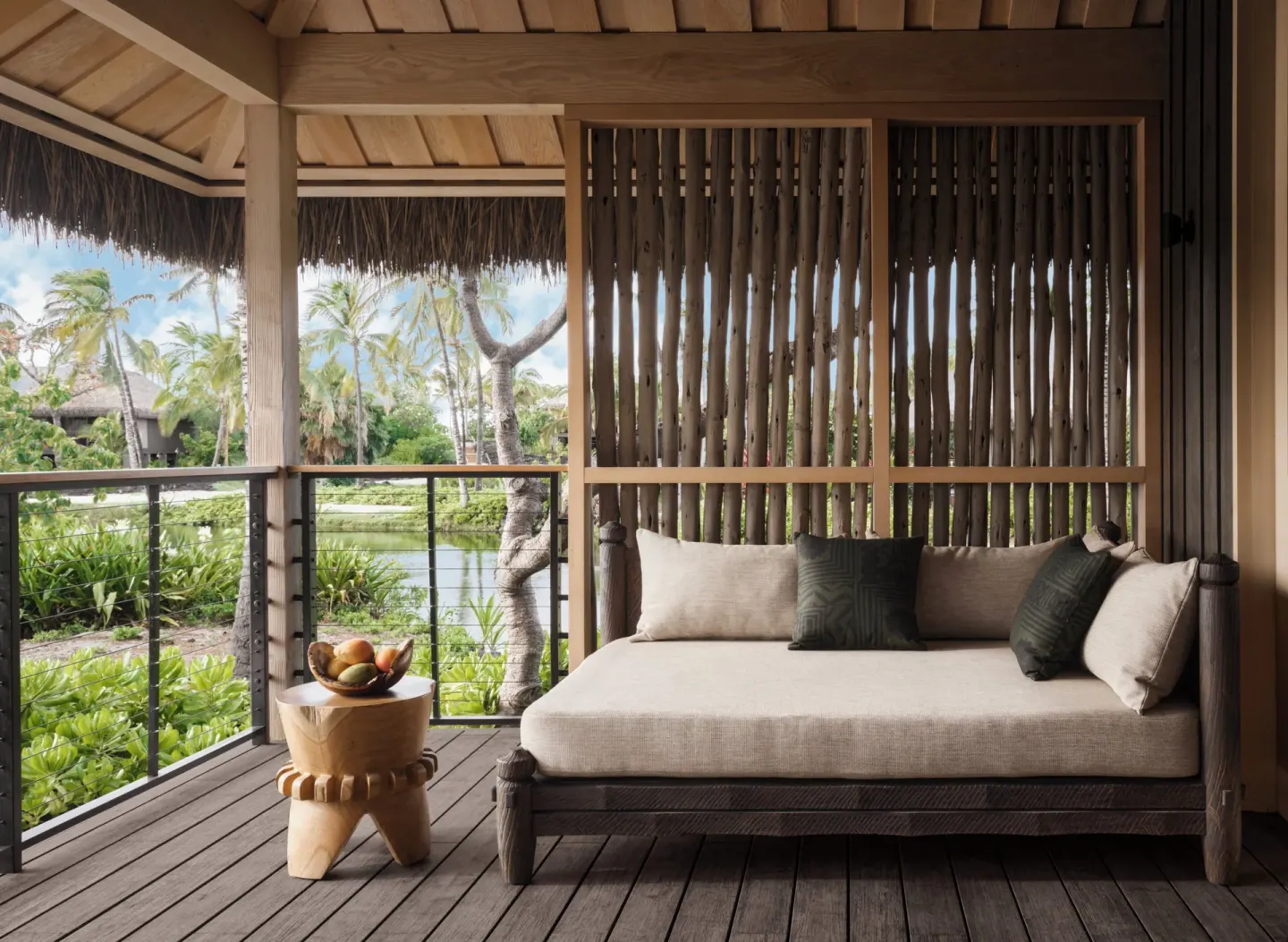 Lagoon view lanai daybed at Kona Village with palms and water beyond the railing.