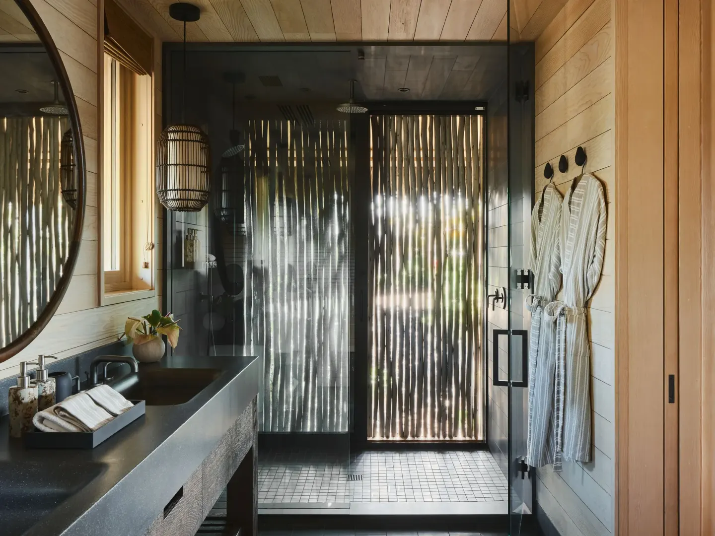 Bathroom with vanity, glass shower, and robes in the Ocean Front Black Sand Two Bedroom Kauhale at Kona Village.