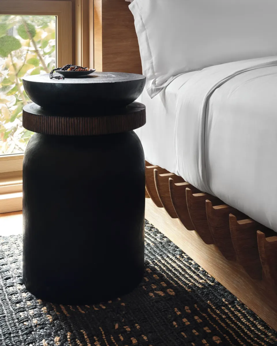 Bedside table and white bed linens in an Ocean Front Black Sand Two Bedroom Kauhale at Kona Village.