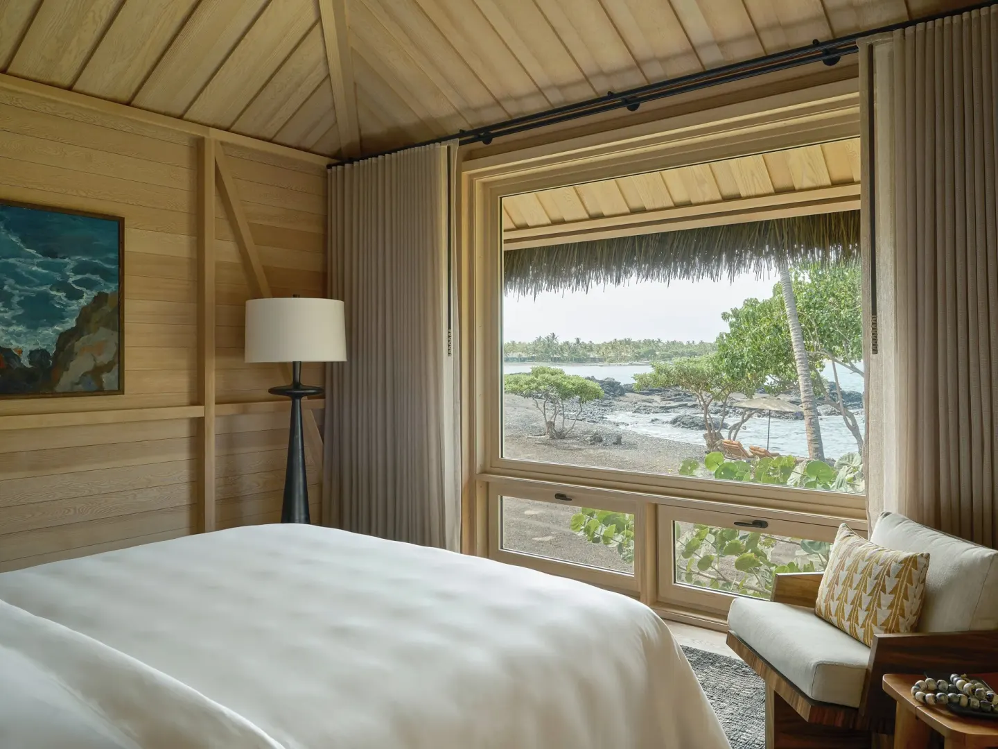 King bed and ocean-facing window in an Ocean Front Black Sand Two Bedroom Kauhale at Kona Village.