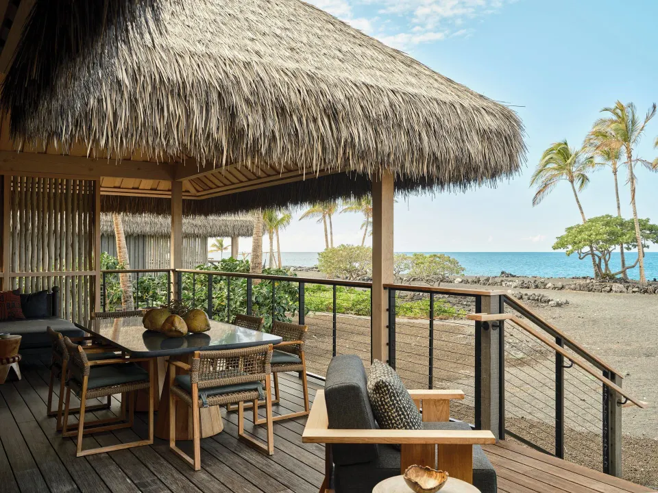 Ocean Front One Bedroom Kauhale lanai with dining table, lounge chairs and ocean view at Kona Village.
