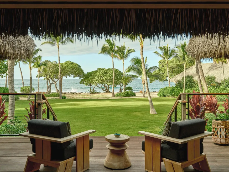 Ocean View One Bedroom Kauhale lanai with chairs facing palms and ocean at Kona Village.