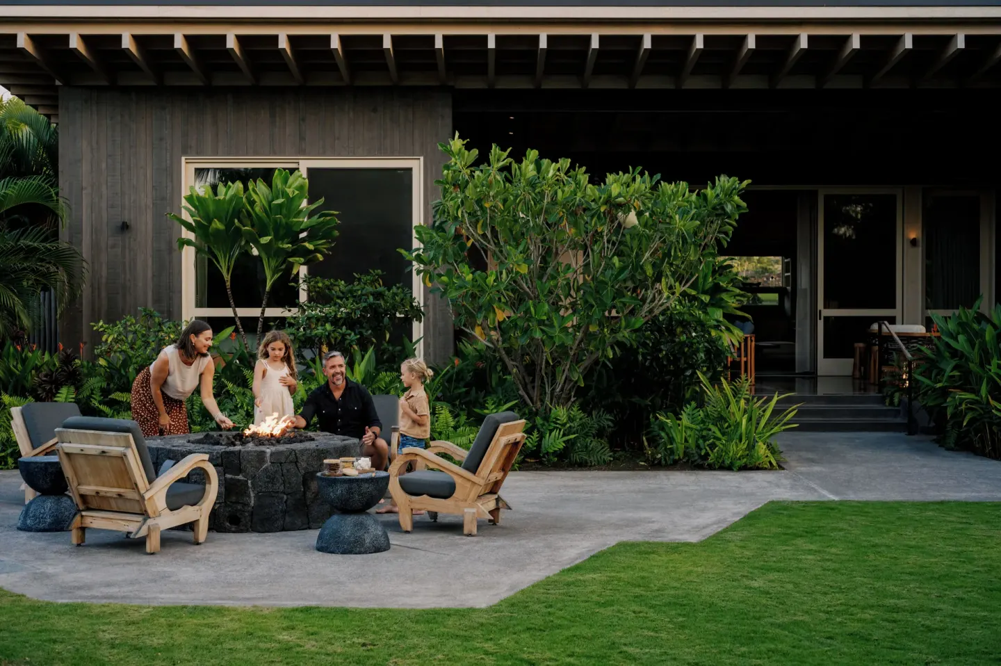 Guests gather around an outdoor fire pit at the Ohana Pool Accessible Four Bedroom Kauhale at Kona Village.