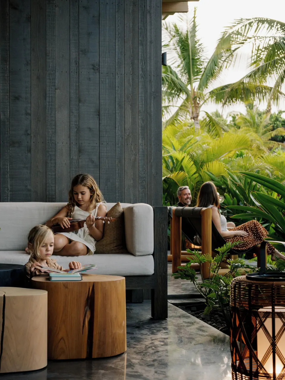 Family relaxes on a covered lanai of the Ohana Room Pool Four Bedroom Kauhale at Kona Village.