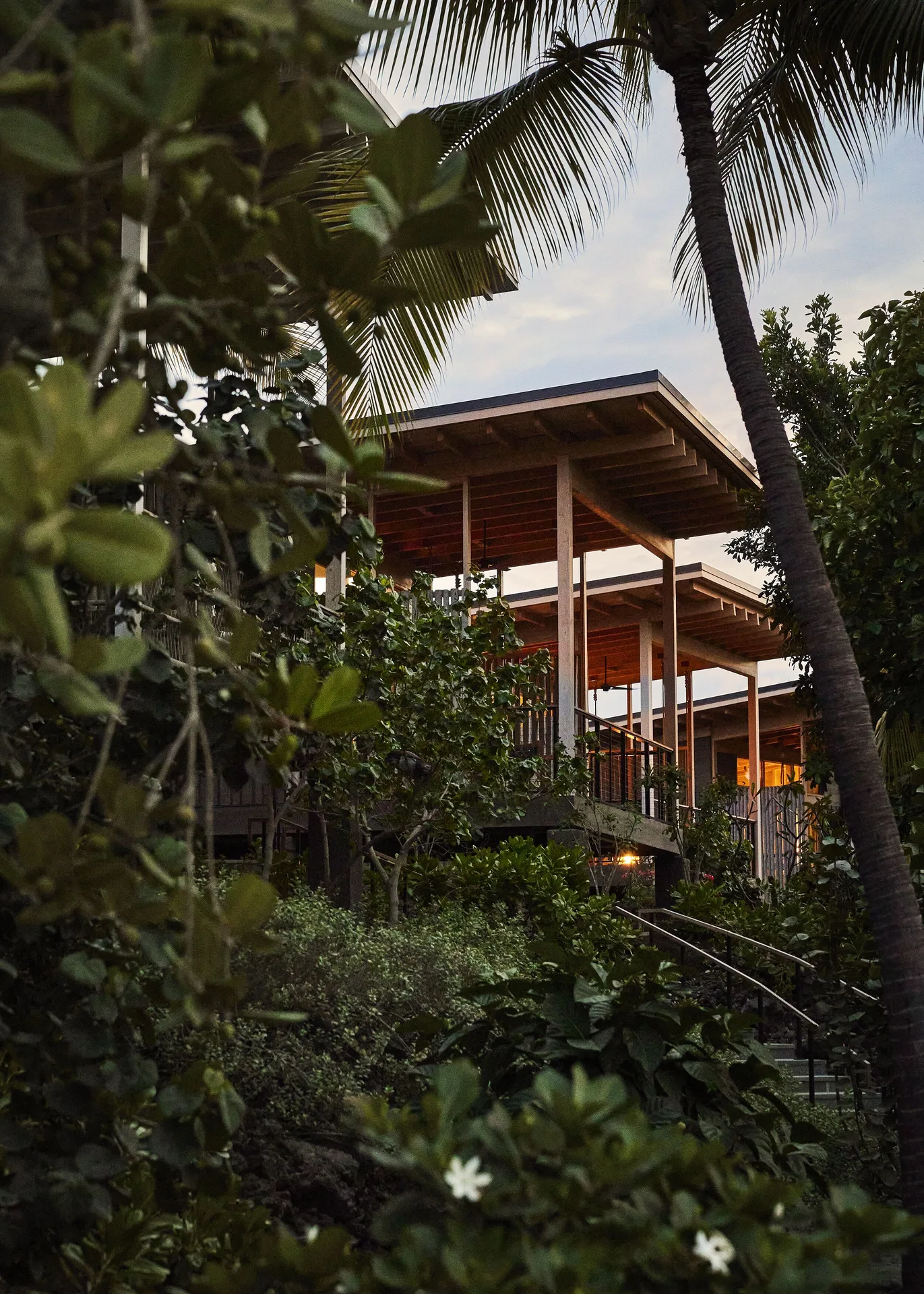Tree Top Hale exterior at Kona Village framed by palms and tropical foliage at dusk.